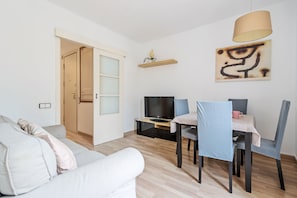 Un salon moderne comprenant un canapé, une table à manger avec des chaises, un téléviseur et une lampe fixée au mur.
