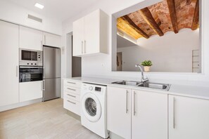 Una cucina moderna con mobili bianchi, forno integrato, lavatrice, lavello e soffitto in mattoni.