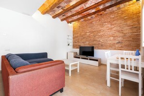 Un soggiorno con divano, televisore, tavolino bianco e sedie.