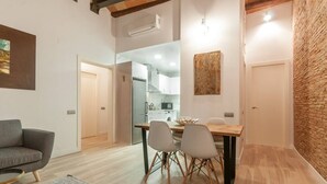 A modern living room with a grey sofa, a wooden dining table with four chairs, and a kitchen visible through an open door. - Unpack your bags, take a deep salty breath, inhale the sea in, and wonder at the magic of Barcelona (Barcelona)