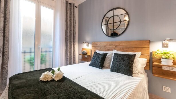 Une chambre avec un grand lit, une tête de lit en bois, un miroir rond, des lampes de chevet et une vue sur l’extérieur grâce à une porte coulissante.