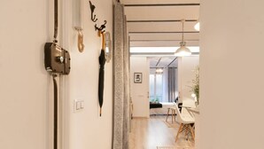 Un couloir avec une porte, un porte-manteau avec un manteau, et un coin repas avec une table et des chaises.
