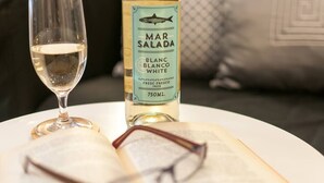 Une bouteille de Mar Salada Blanc Blanco White est posée sur une table, à côté d’un verre de vin blanc et d’une paire de lunettes.