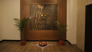 A reception area with a wooden panel wall, a marble plaque with the hotel name, two potted plants, and a decorative bowl on the floor. - Sky suites by Monarch (Navi Mumbai)