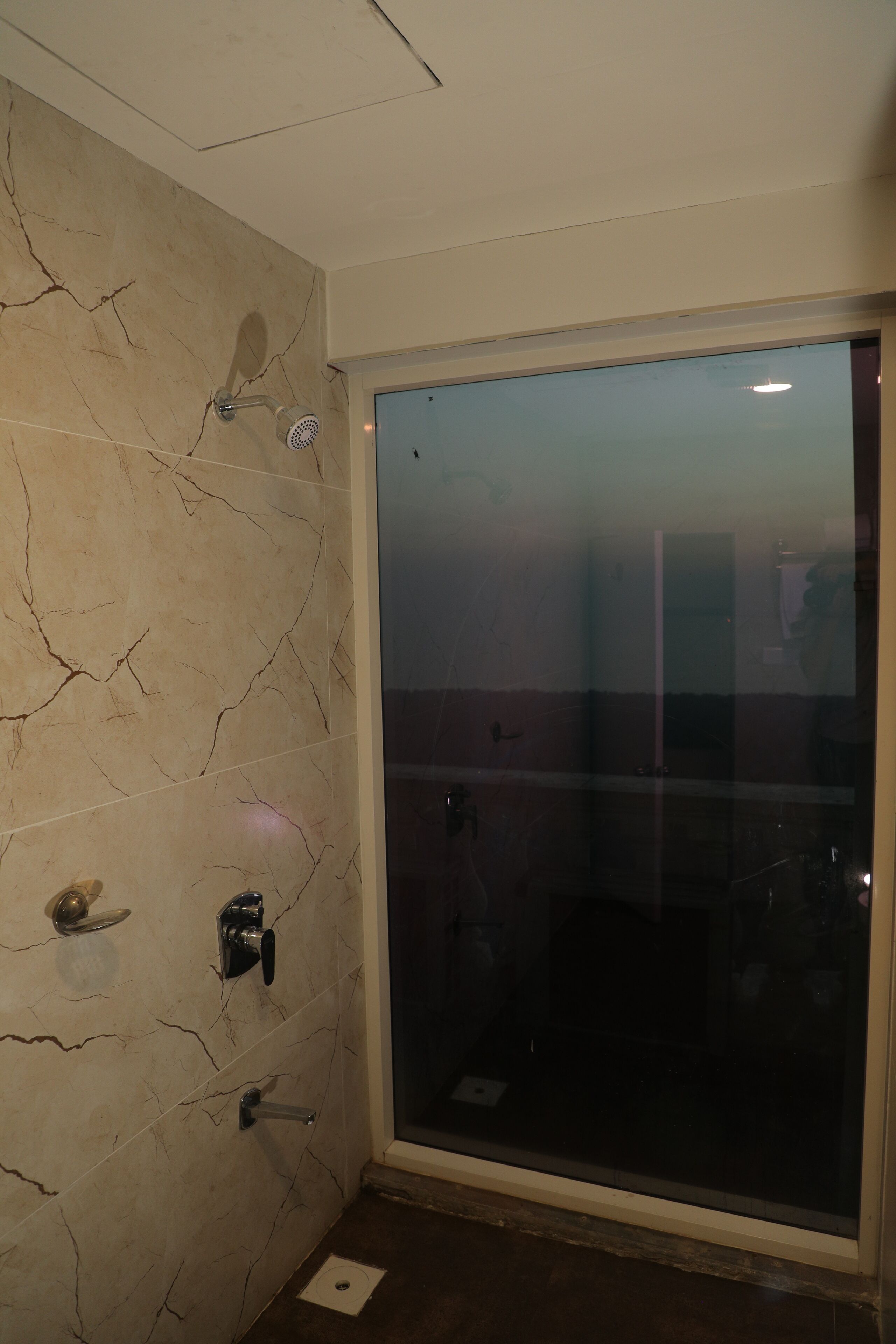 A bathroom with a glass shower door, a marble wall, and a toilet.