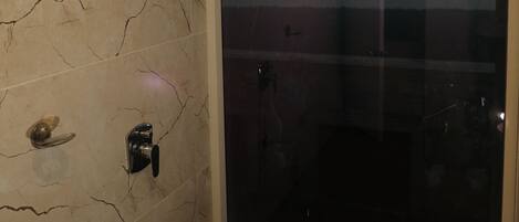 A bathroom with a glass shower door, a marble wall, and a toilet.