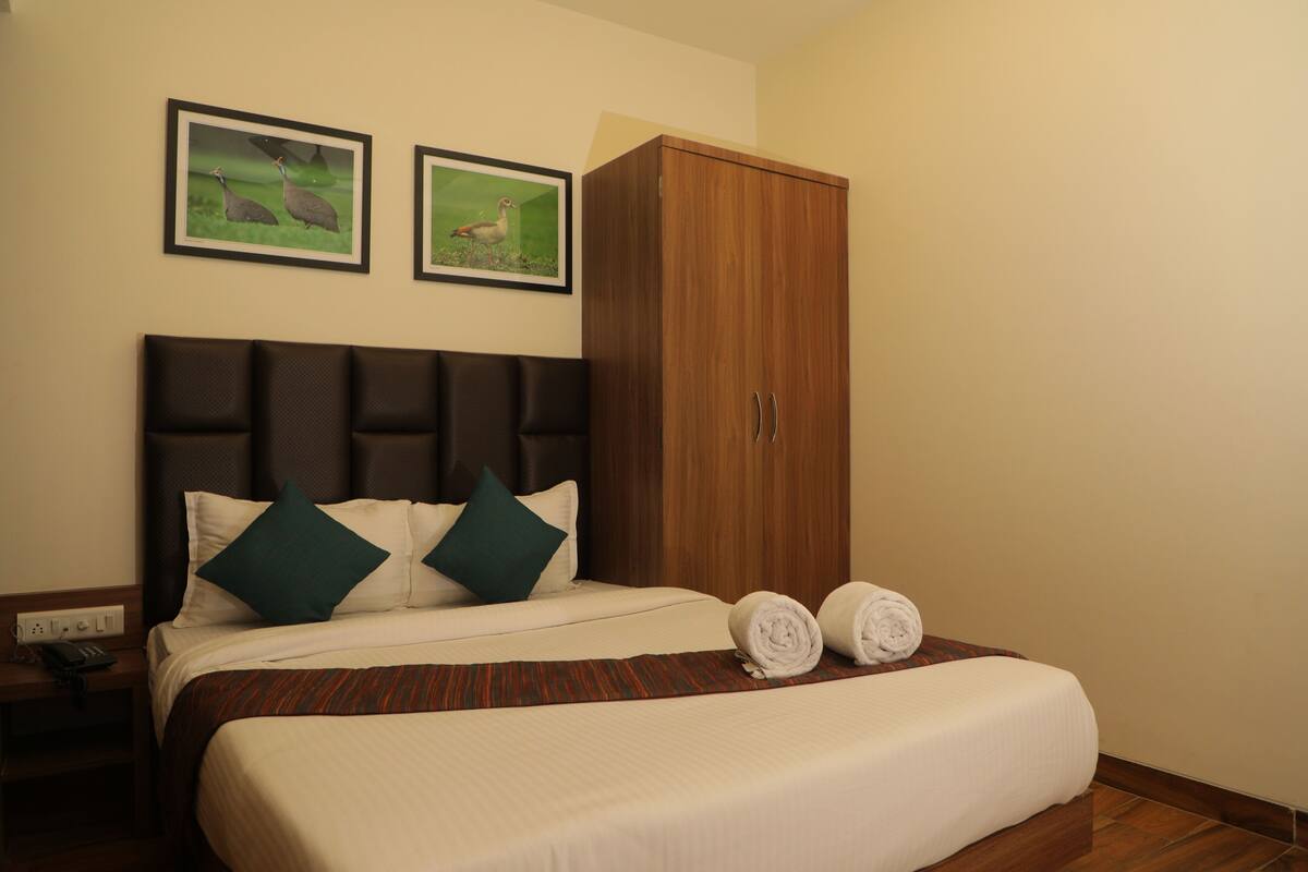 Quarto de hotel com uma cama, um guarda-roupa de madeira e duas fotografias emolduradas na parede.