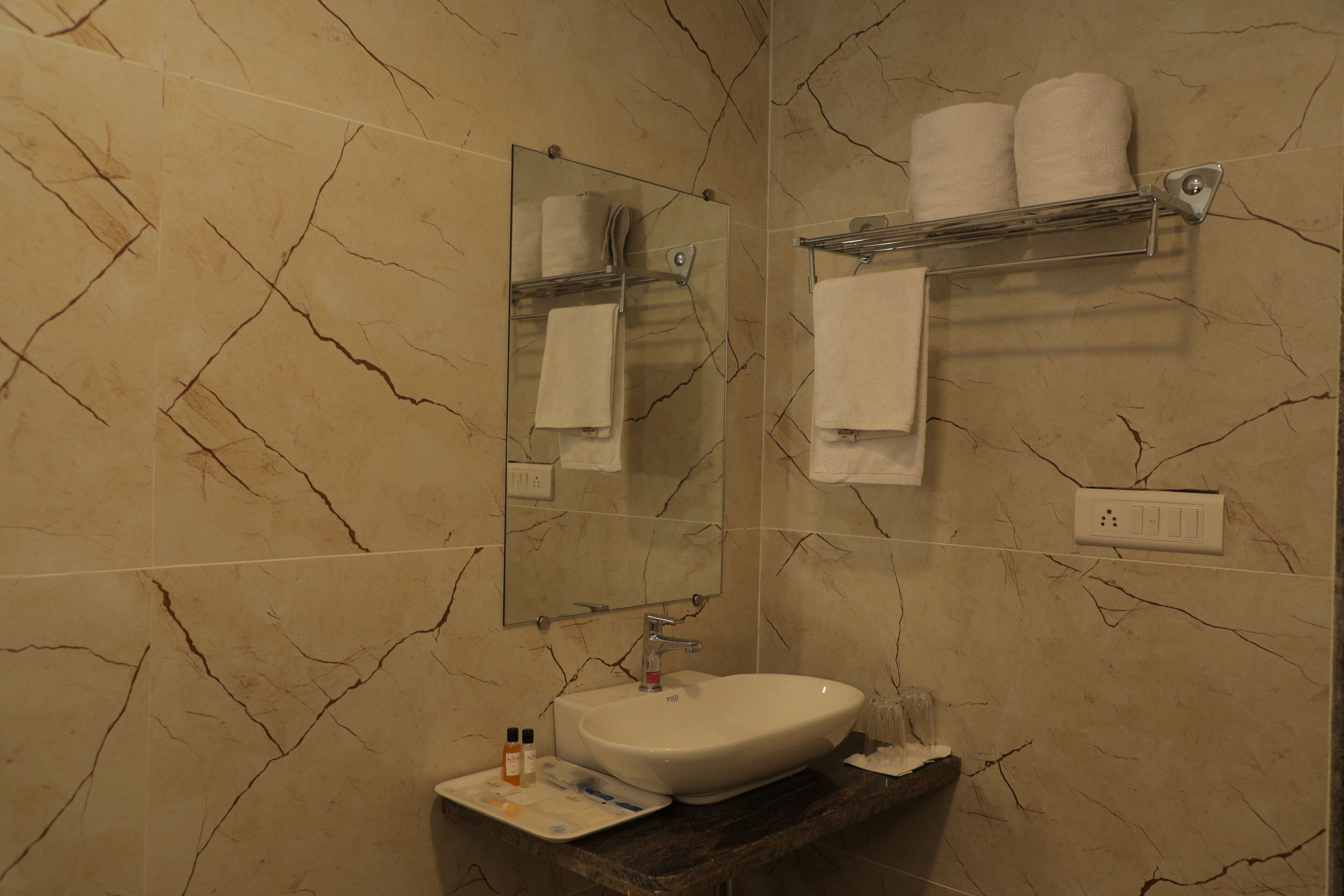Une salle de bain avec un mur recouvert de carreaux de marbre, un lavabo avec un miroir au-dessus et un porte-serviettes avec deux serviettes.