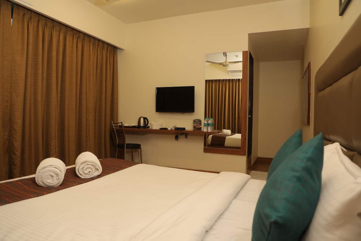 Quarto de hotel com uma cama grande, televisão de tela plana na parede, escrivaninha com cadeira e um espelho refletindo o quarto.