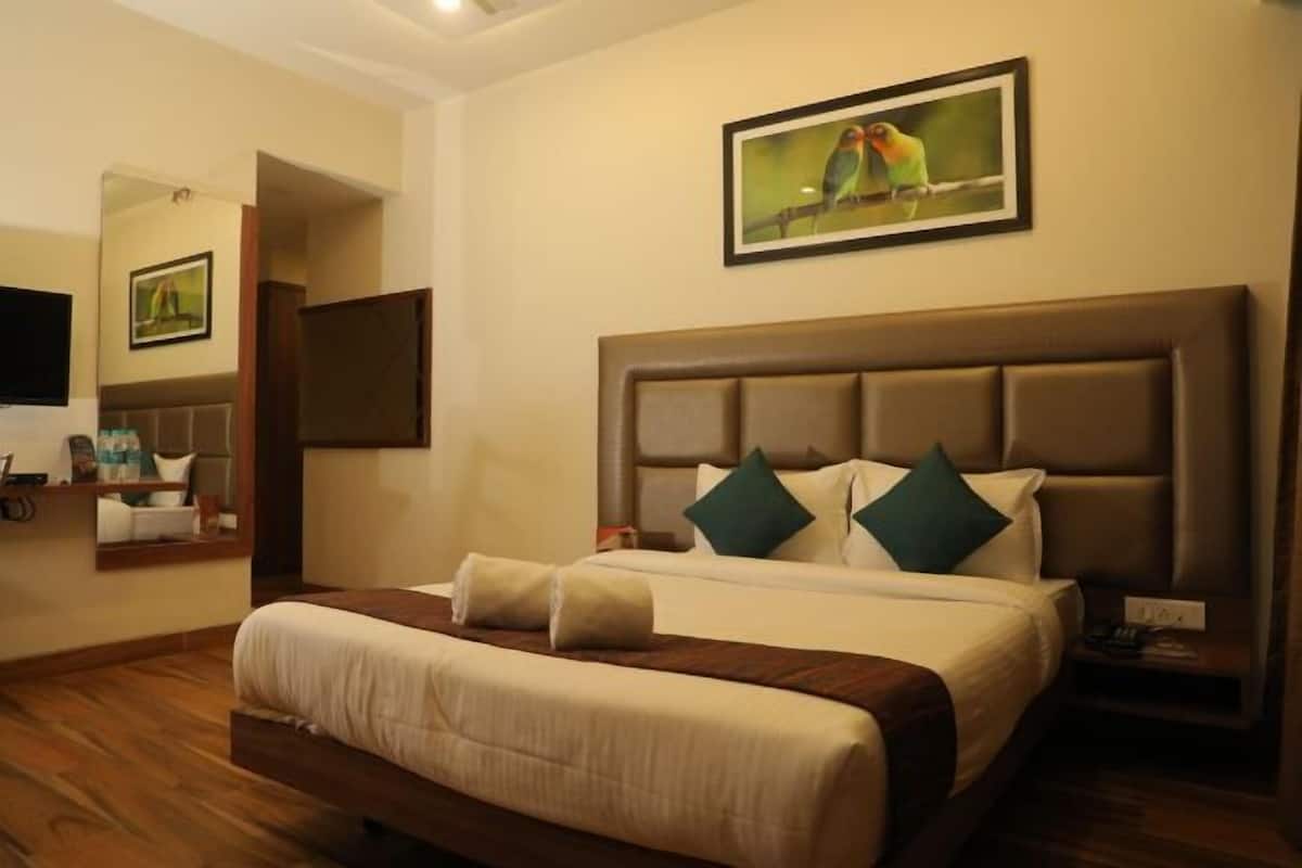 Quarto de hotel com cama grande, televisão, pintura de pássaros e chão de madeira.