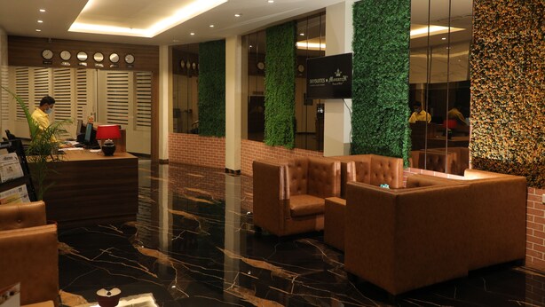 A hotel lobby with a reception desk, seating area, and a green wall with a clock. - Sky suites by Monarch (Navi Mumbai)
