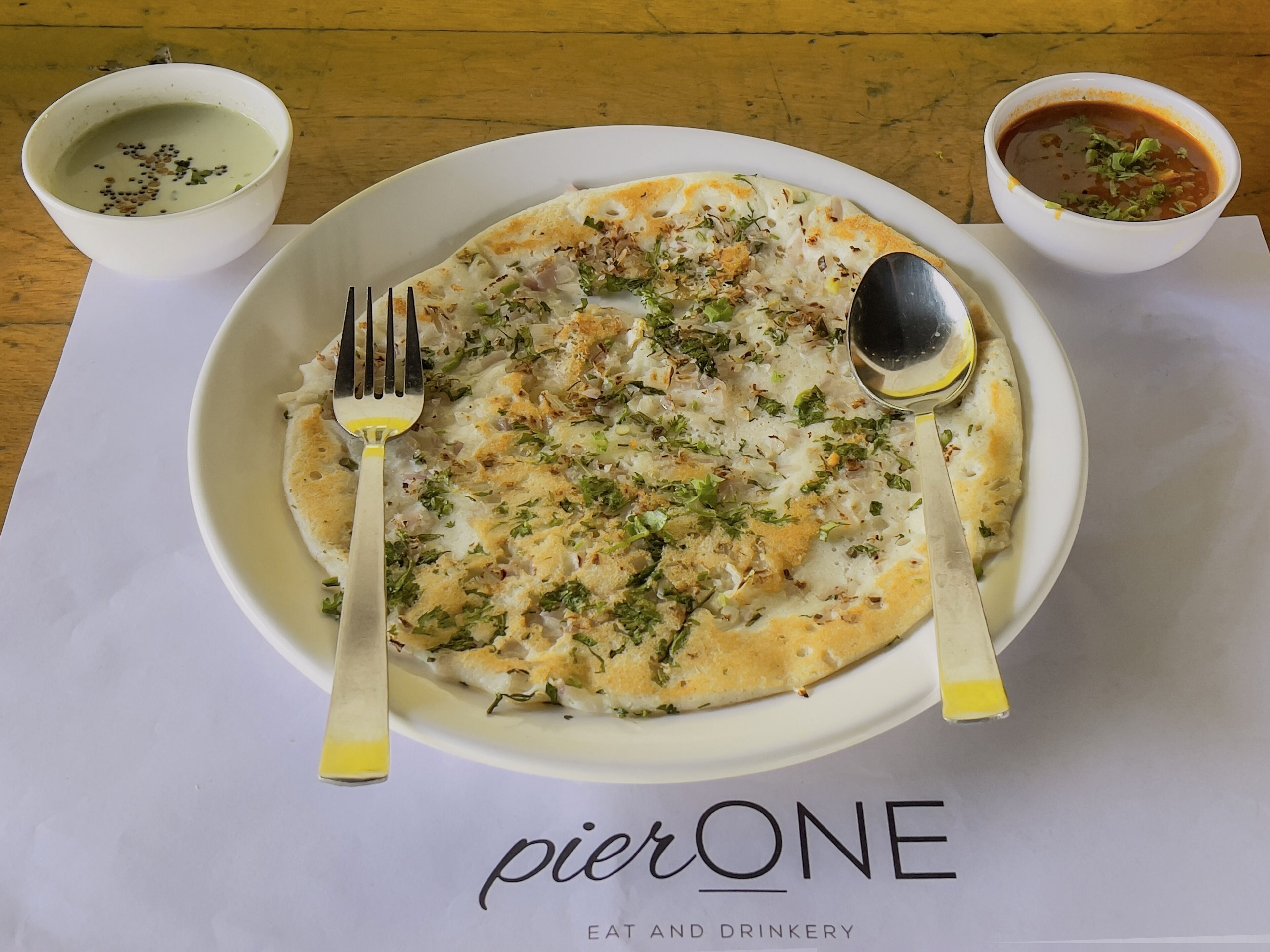 Prato de comida com garfo e colher sobre uma mesa com jogo americano identificado como "pierONE".