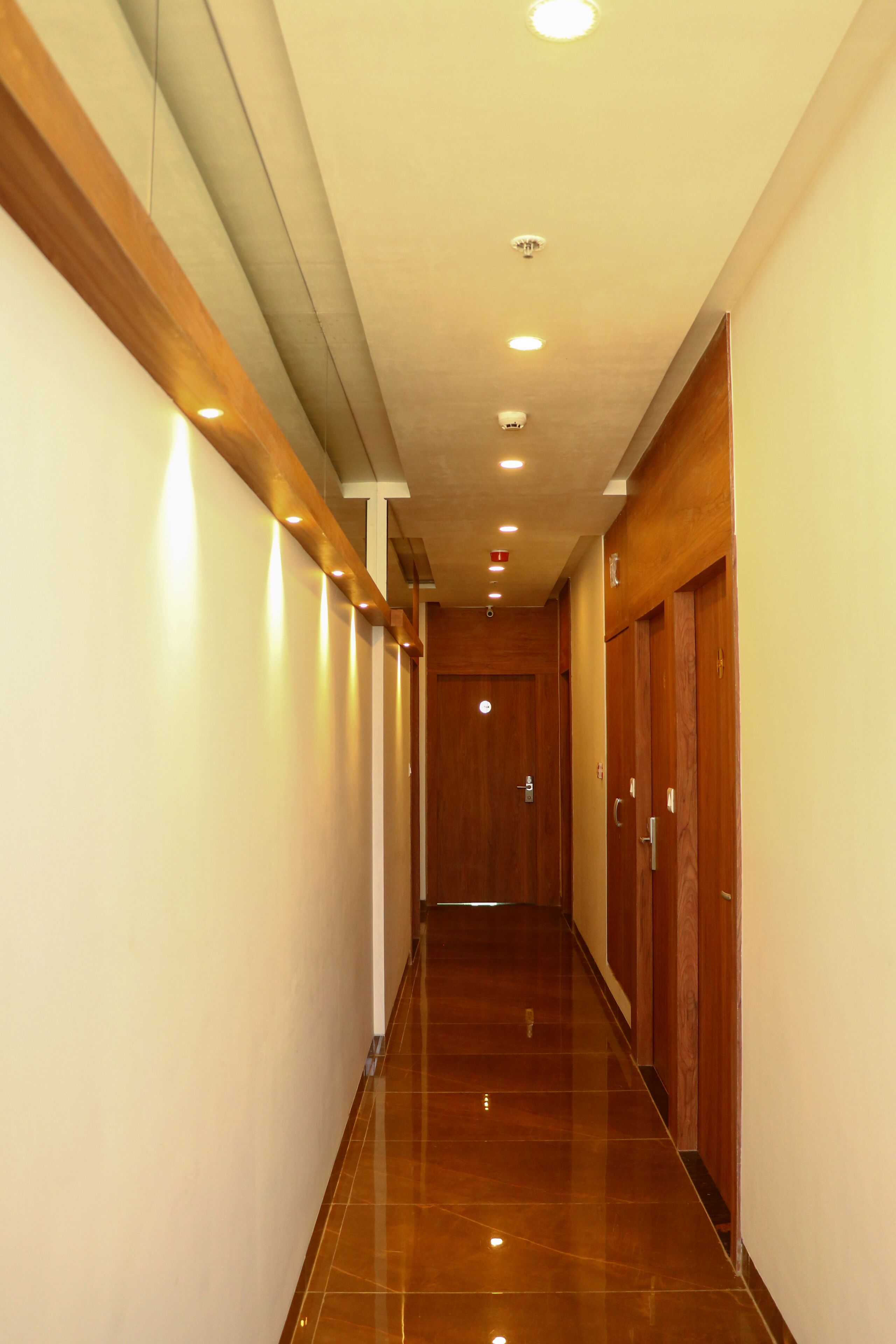 Un pasillo con puertas de madera, paredes blancas y un piso de baldosas brillantes.