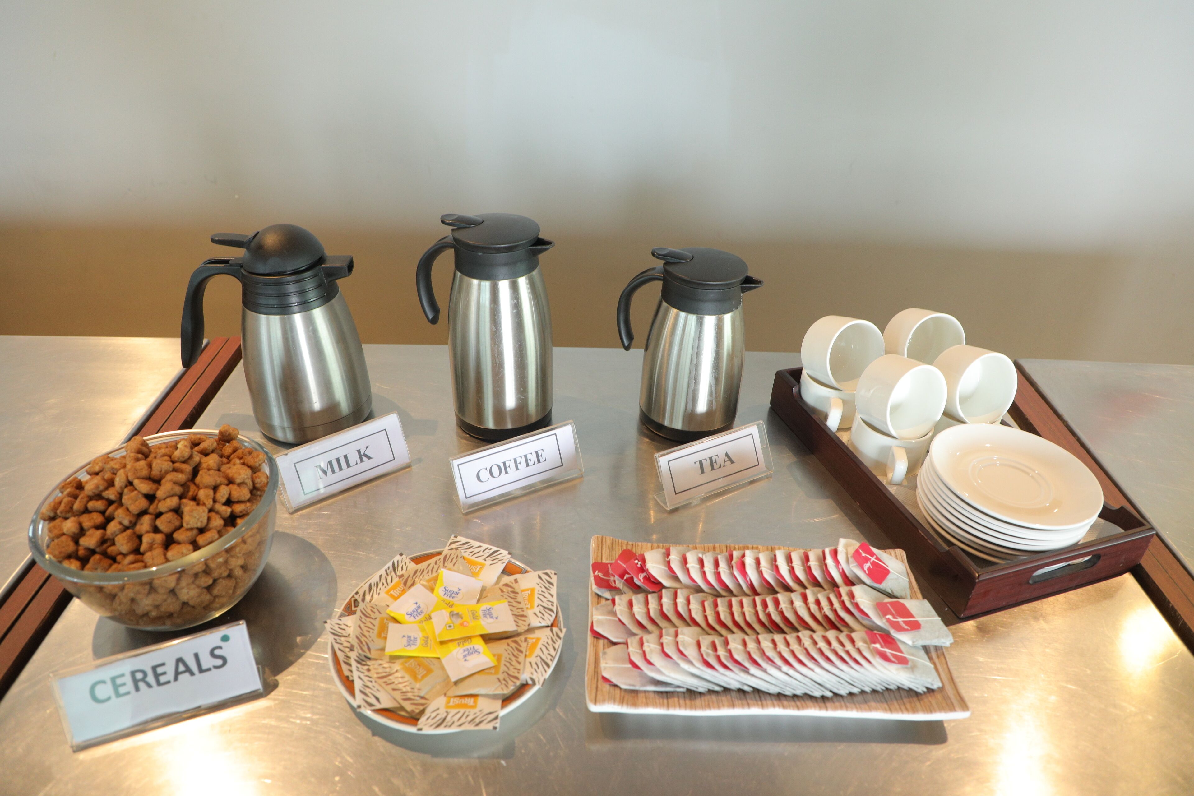 A breakfast buffet with labeled containers for milk, coffee, tea, cereals, and pastries.