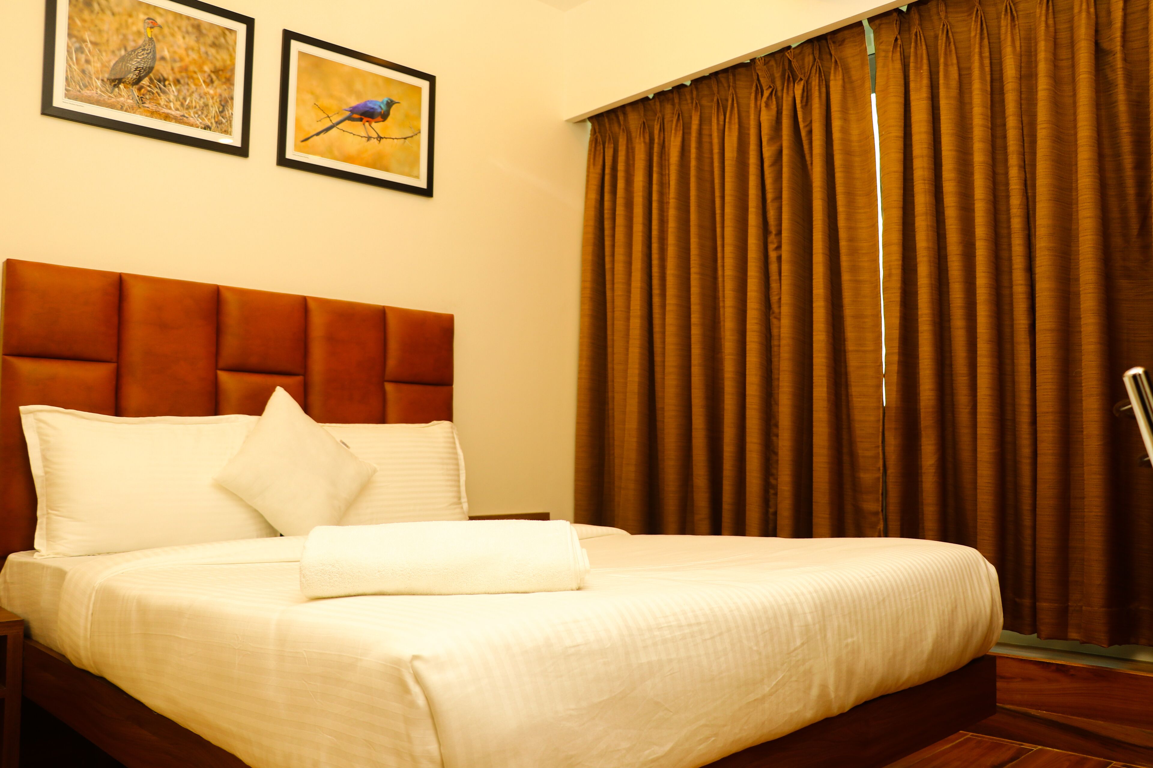 A hotel room with a large bed, a wooden headboard, and two framed pictures on the wall.