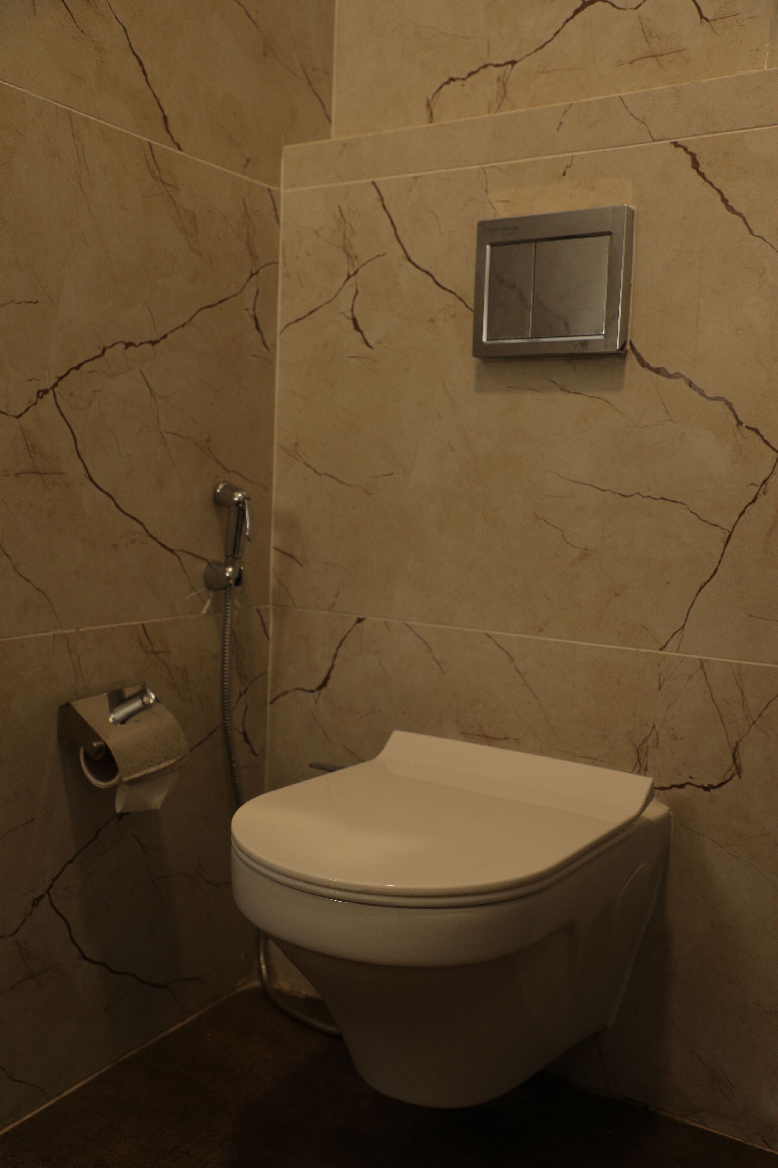 Un baño con inodoro, dispensador de toallas de papel y cabezal de ducha en la pared.