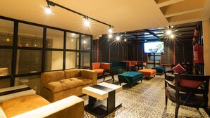 A modern lounge area with sofas, a coffee table, and a TV screen. - Shubham Vilas - Hostel (New Delhi)