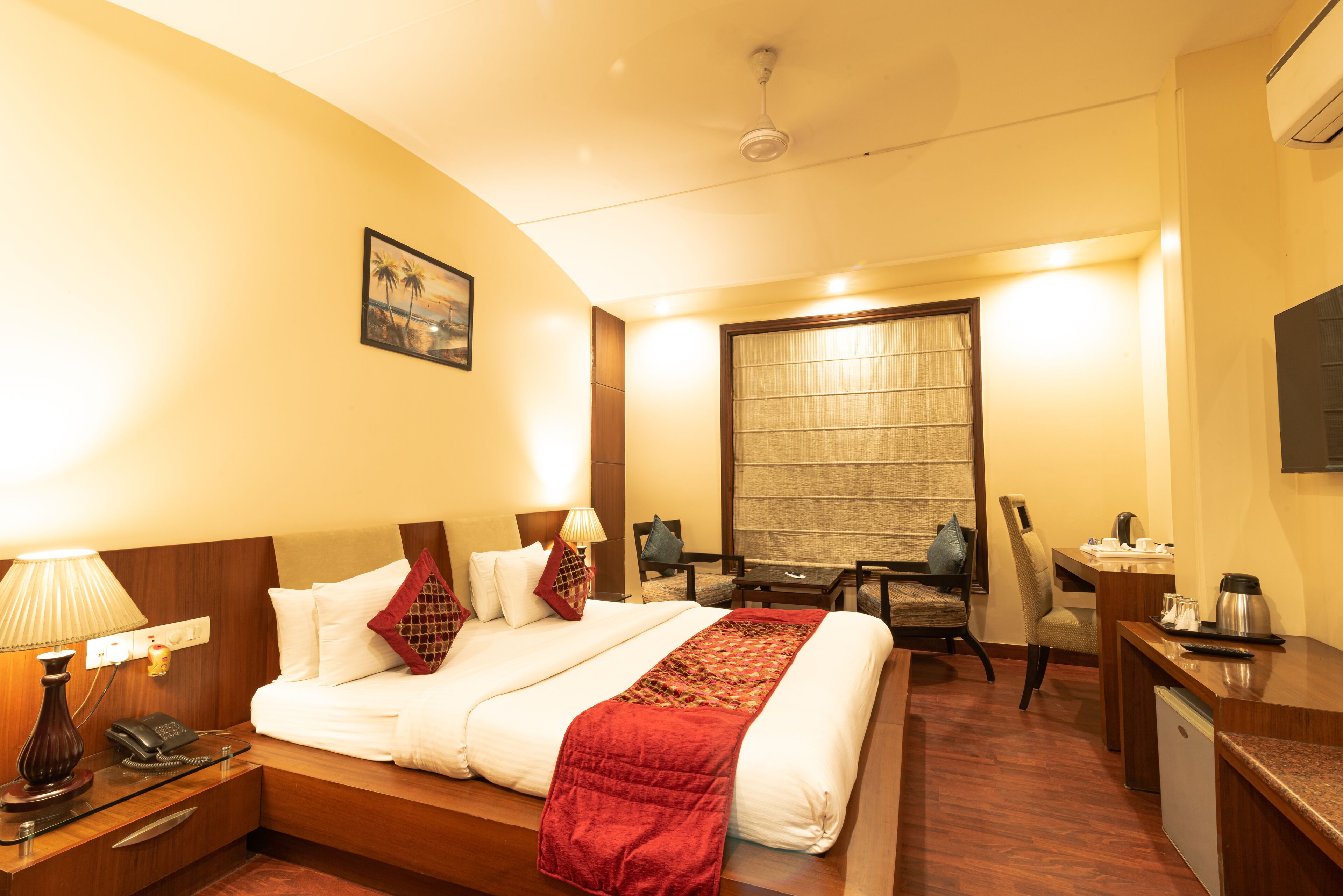 A hotel room with a bed, bedside table, lamp, desk, chair, and a television.