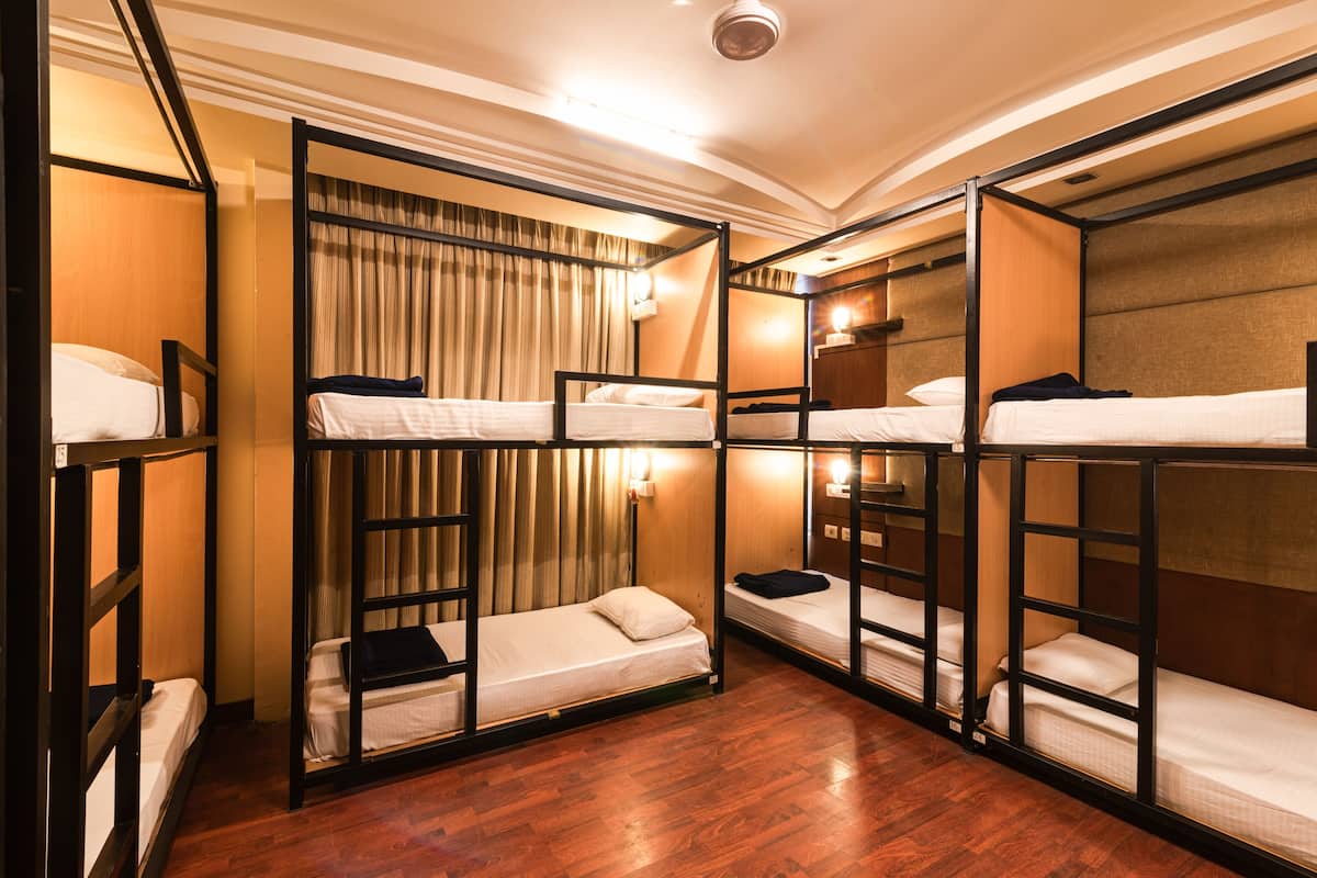 A room with bunk beds, wooden flooring, and a curtain on the window.