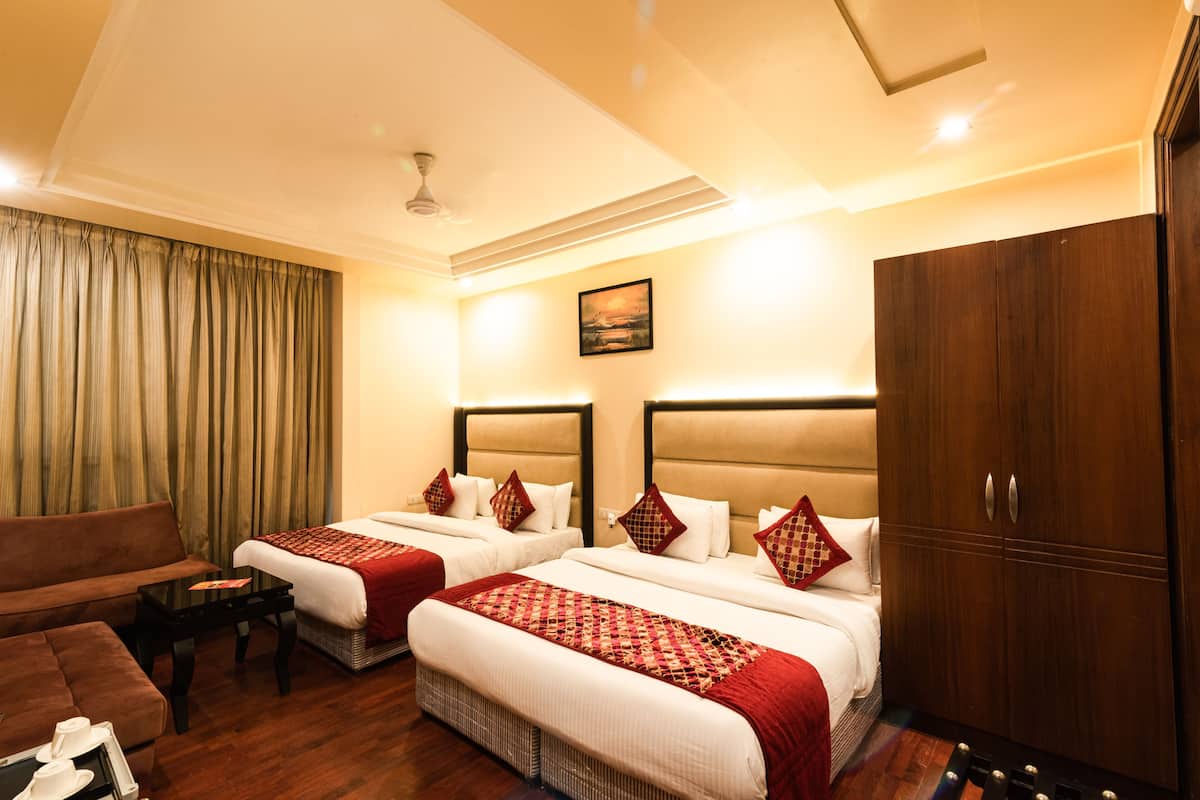 A hotel room with two beds, a sofa, a wooden wardrobe, and a ceiling fan.