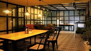 A cozy dining area with a wooden table and chairs, a coffee pot, and hanging pendant lights. - Shubham Vilas - Hostel (New Delhi)