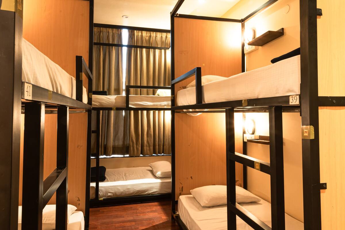 A narrow hallway with bunk beds, wooden walls, and a window with curtains.