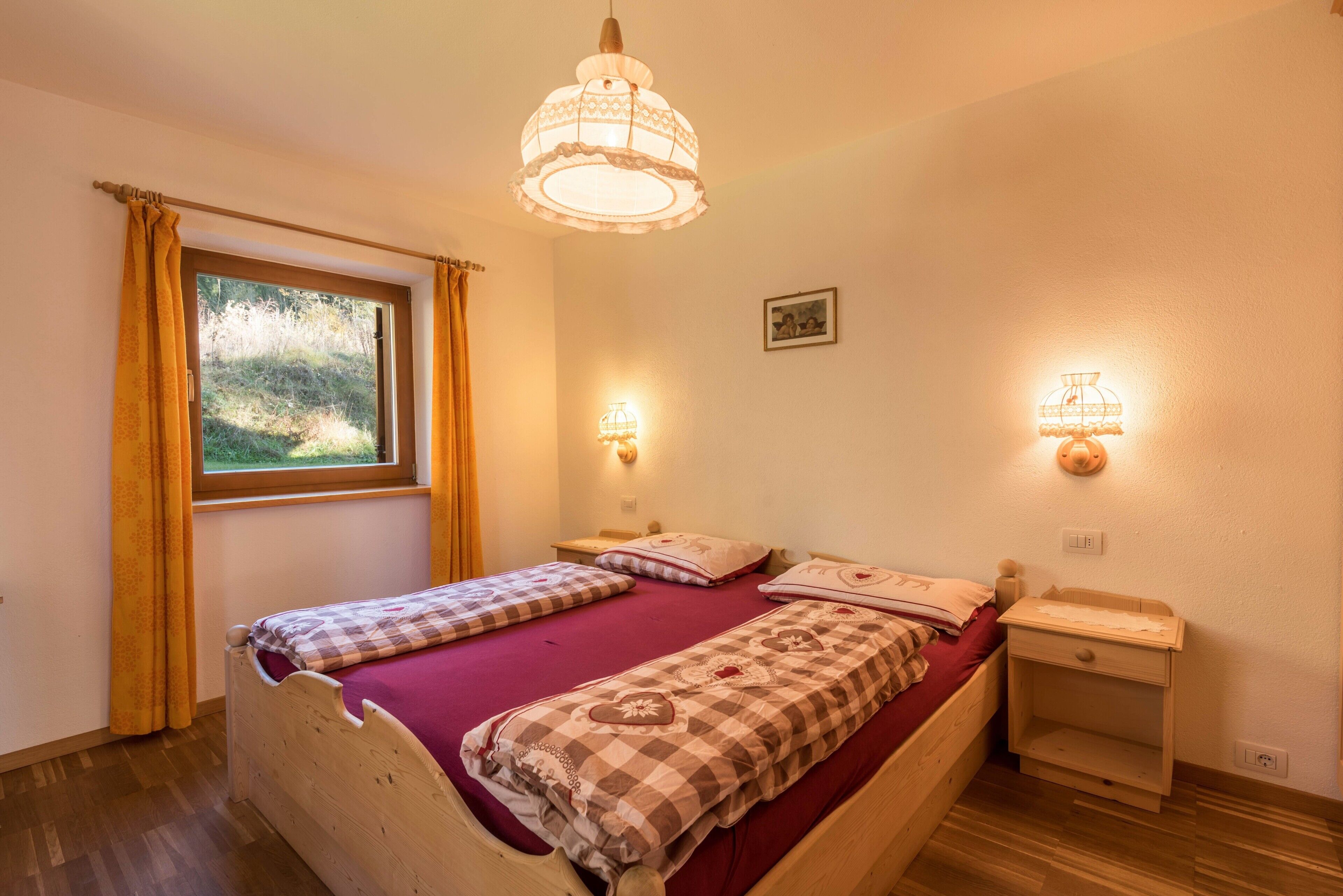 A bedroom with a wooden bed, two bedside tables, a window with curtains, and wall-mounted lamps.
