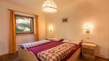 A bedroom with a wooden bed, two bedside tables, a window with curtains, and wall-mounted lamps.