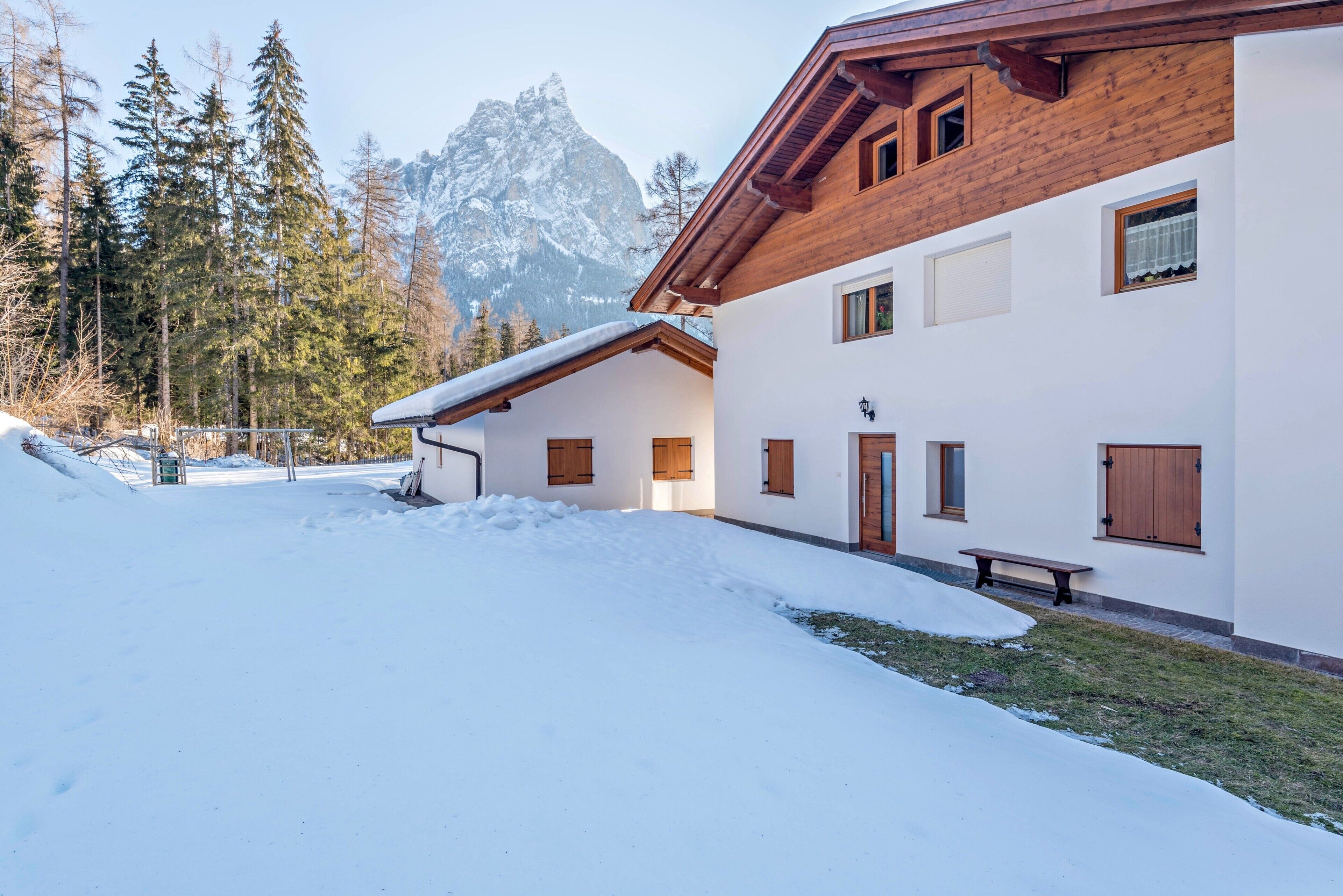 A snow-covered building with a wooden exterior, a bench, and a mountain in the background.