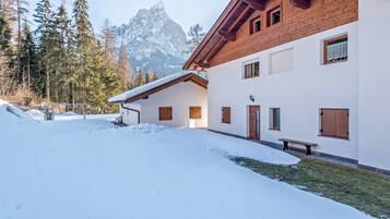 A snow-covered building with a wooden exterior, a bench, and a mountain in the background.