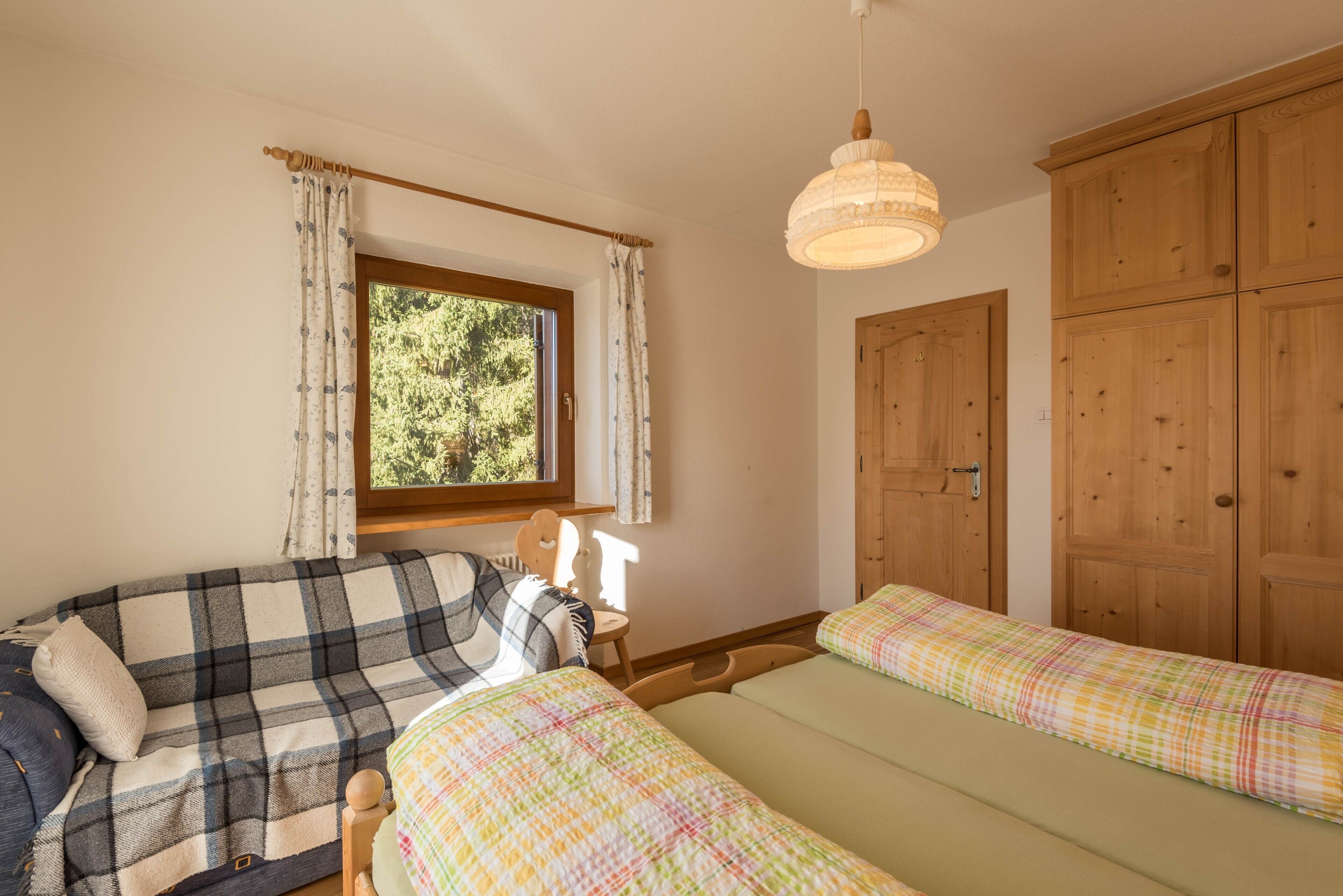 Una habitación con dos camas, una ventana con cortinas, un armario de madera y una lámpara colgante.