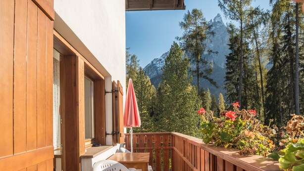 A wooden deck with a table and chairs, a red umbrella, and a view of a mountain range.