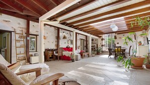 Una zona d'estar oberta amb un sostre alt, bigues de fusta i un paviment de rajola.
