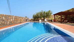 Una piscina amb mur de pedra, gandules i una pèrgola.
