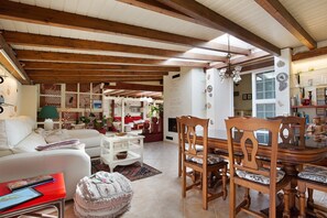 A spacious living area with a wooden ceiling, a dining table with chairs, a white sofa, and a red coffee table.