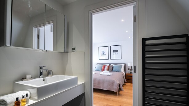 Uma casa de banho moderna com uma grande pia e espelho, um closet espaçoso e um quarto com cama e mesa de cabeceira.