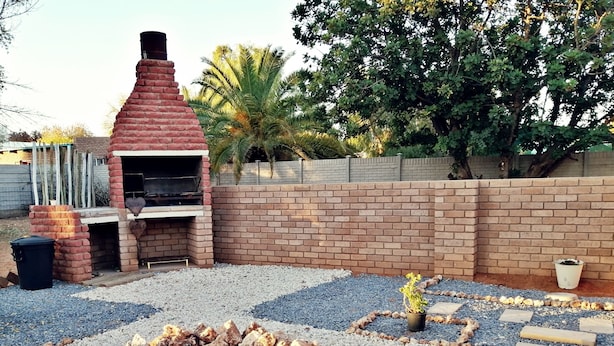 A backyard with a brick fireplace, a stone fire pit, and outdoor seating. - Ambiente Budget Accommodation (Upington)