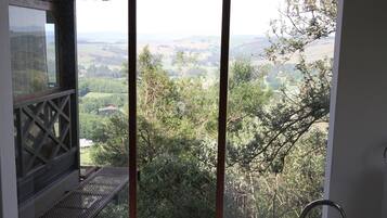 Un baño moderno con una bañera independiente, vistas a un paisaje exuberante y un balcón con techo de paja.