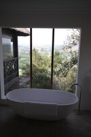 Un baño moderno con una bañera independiente, vistas a un paisaje exuberante y un balcón con techo de paja.