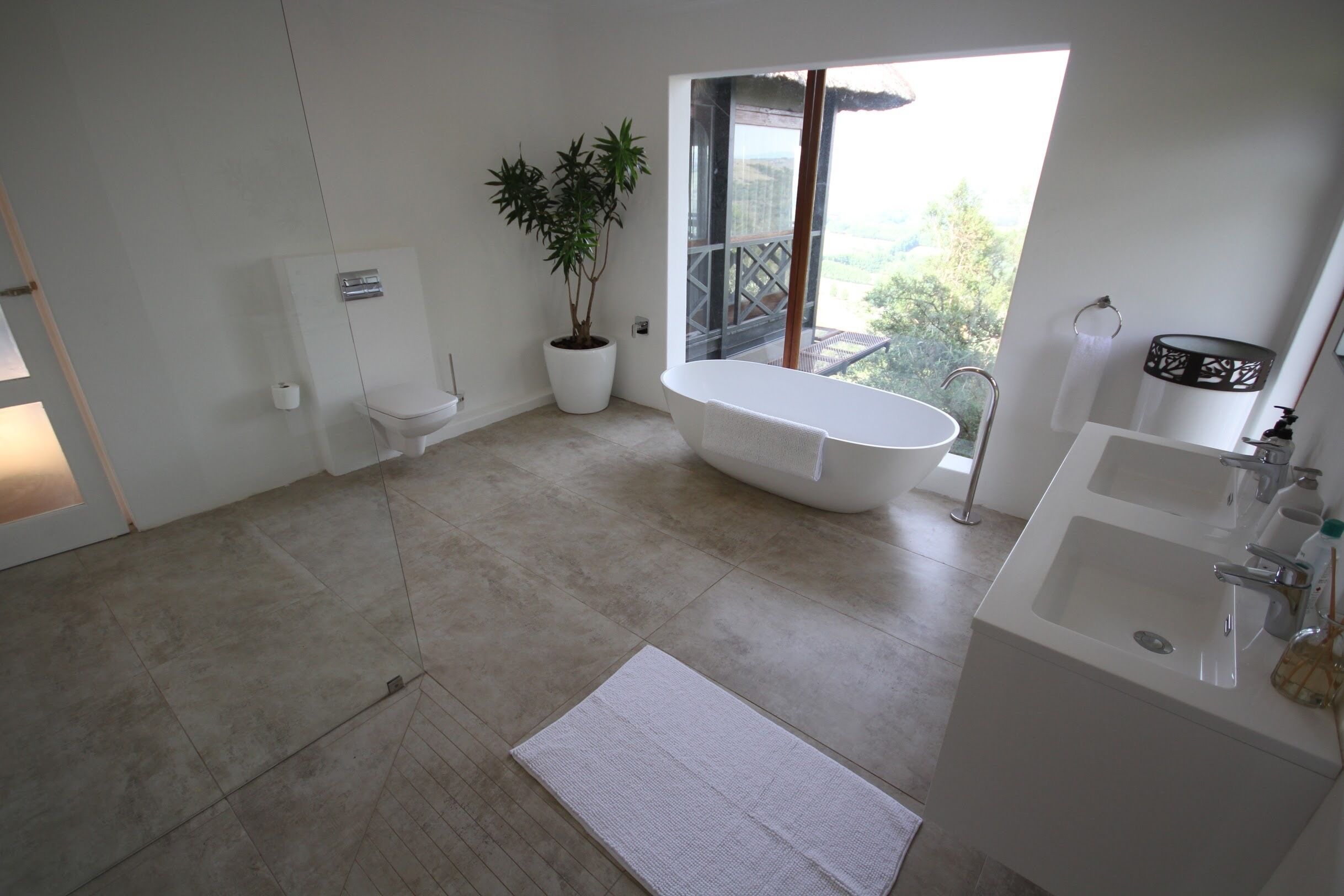 Un baño moderno con bañera, una planta grande en maceta y vistas al exterior.