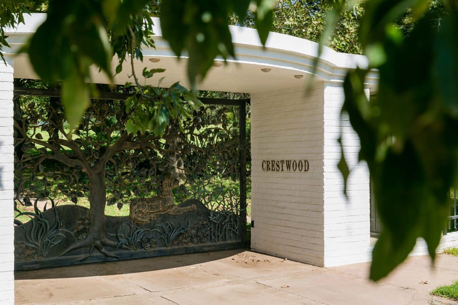Una entrada protegida por un portón con un árbol y una cerca metálica. El portón tiene la leyenda 'Crestwood'.