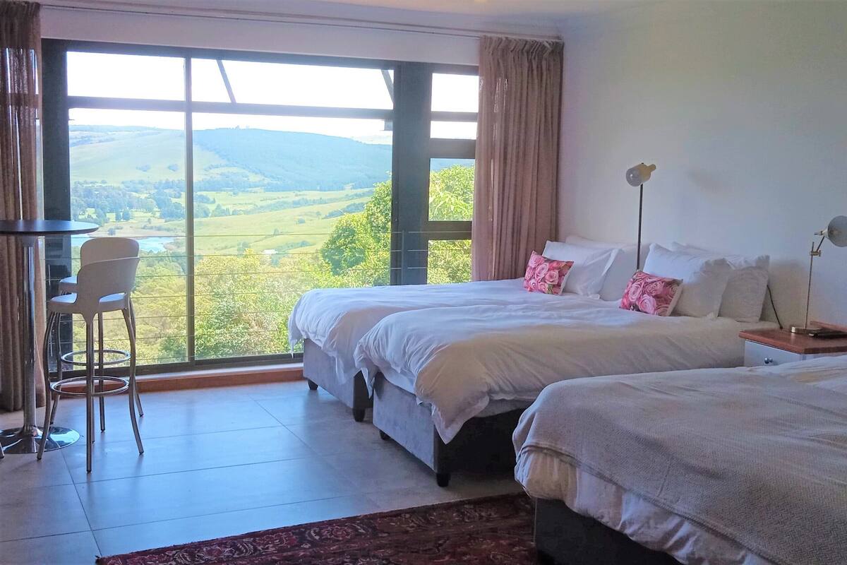 A bedroom with two beds, a chair, a nightstand, and a view of the countryside.