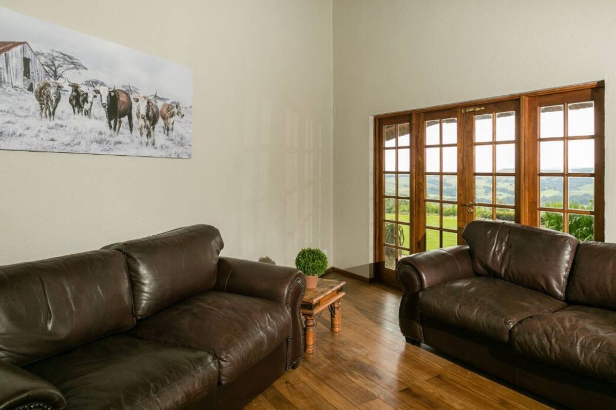 A room with two brown leather sofas, a wooden coffee table, and a painting of cattle on the wall.