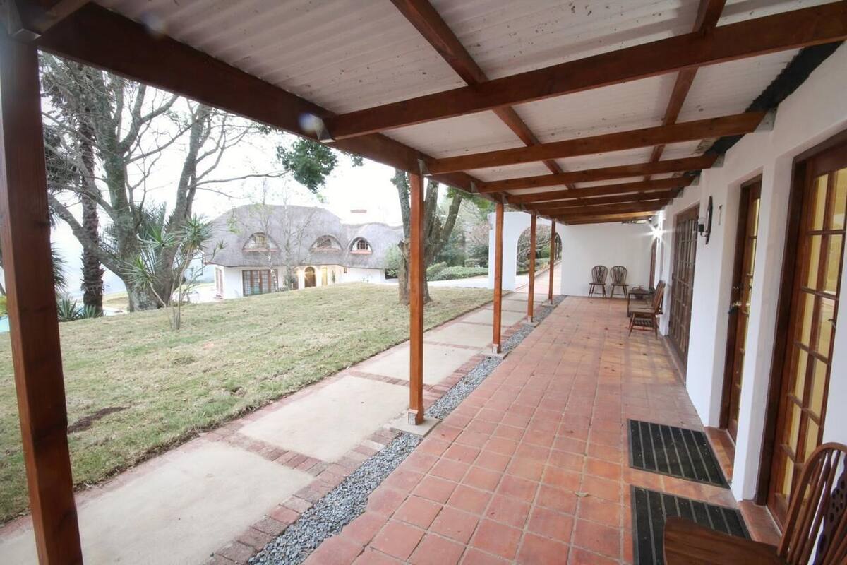 A covered patio with a tiled floor, wooden beams, and a view of a house in the background.