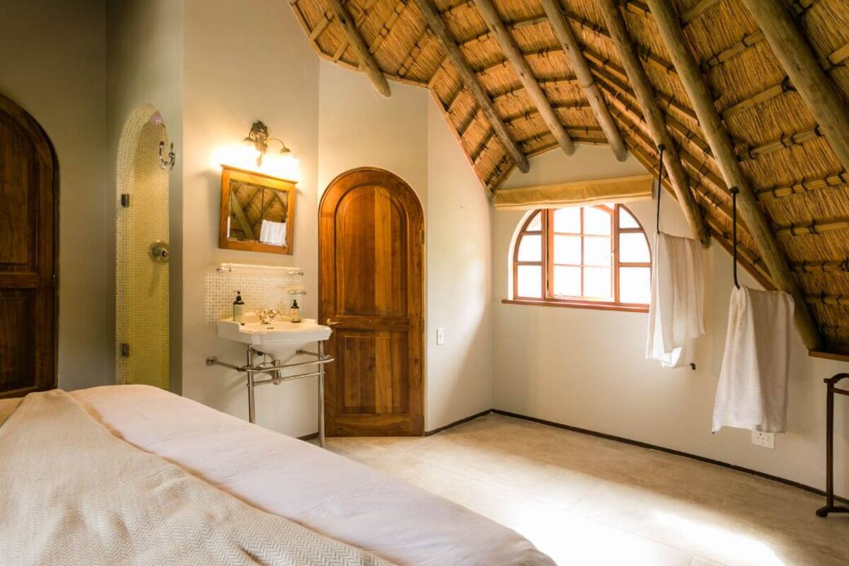 A bedroom with a bed, a wooden door, a window, and a bathroom with a sink and mirror.