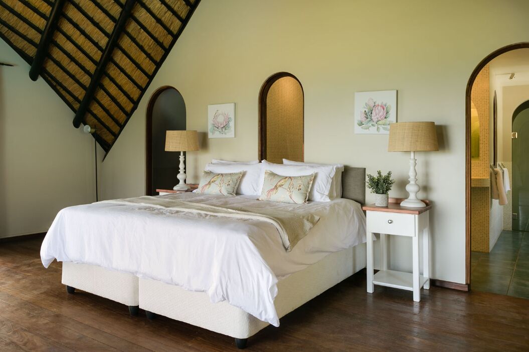 Un dormitorio con una cama grande, dos mesitas de noche con lámparas, un espejo y obras de arte en las paredes.