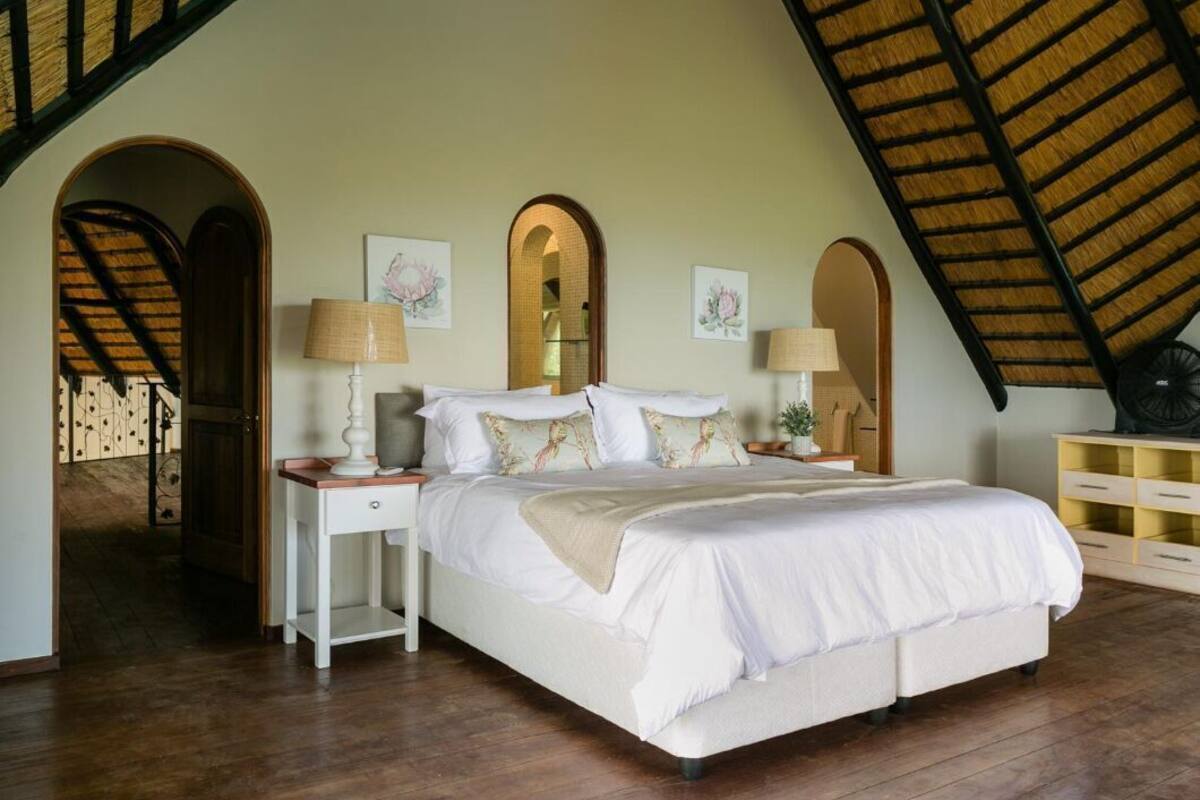 A bedroom with a bed, nightstands, lamps, and a mirror. There are arched doorways and a sloped ceiling.
