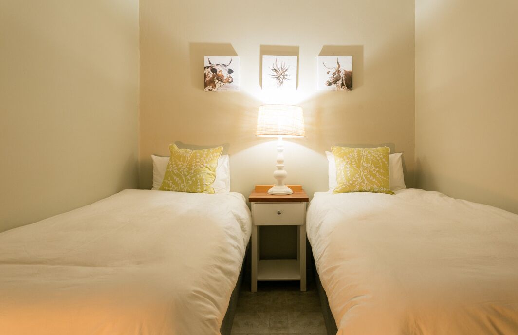 Habitación doble con dos camas, una mesita de noche, una lámpara y cuadros en la pared.