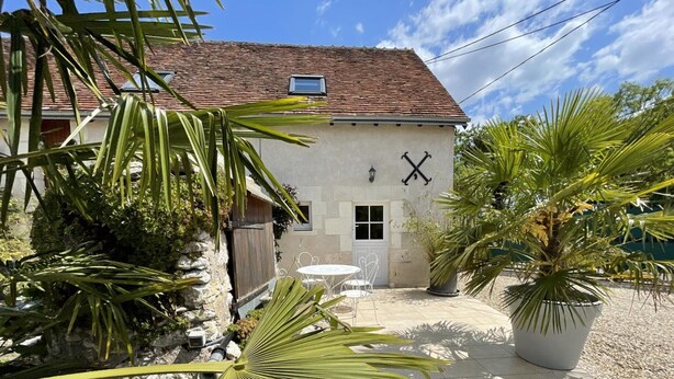 A building with a tiled roof, a small window, and a door. There is a white table and chairs outside.