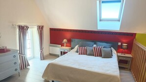 A bedroom with a large bed, a nightstand, a dresser, a window, and a red accent wall.